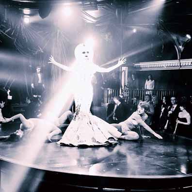 Queen of the night wearing her mask created by Stanley  Allan Sherman.  Blask and white photo, in her dress showing the full face back of the mask, with her arms and hands out to the side.