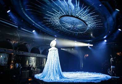 Katherine Crockett in Queen of the night mask standing on stage with a blue light