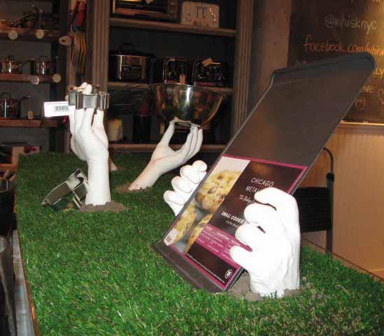 Six plaster cast hand sand arms holding up cookie making kitchen tools, coming out of the grass for a Halloween Display.